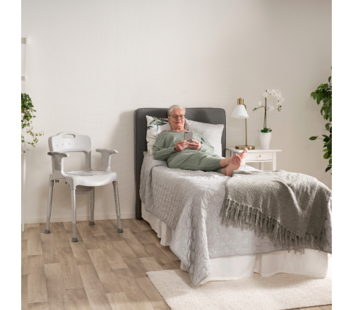 Etac Swift Commode douche-/toiletstoel. (afgebeeld naast een bed)